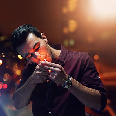 Buy stock photo Shot of a young man lighting a cigarette while standing in the balcony of a nightclub