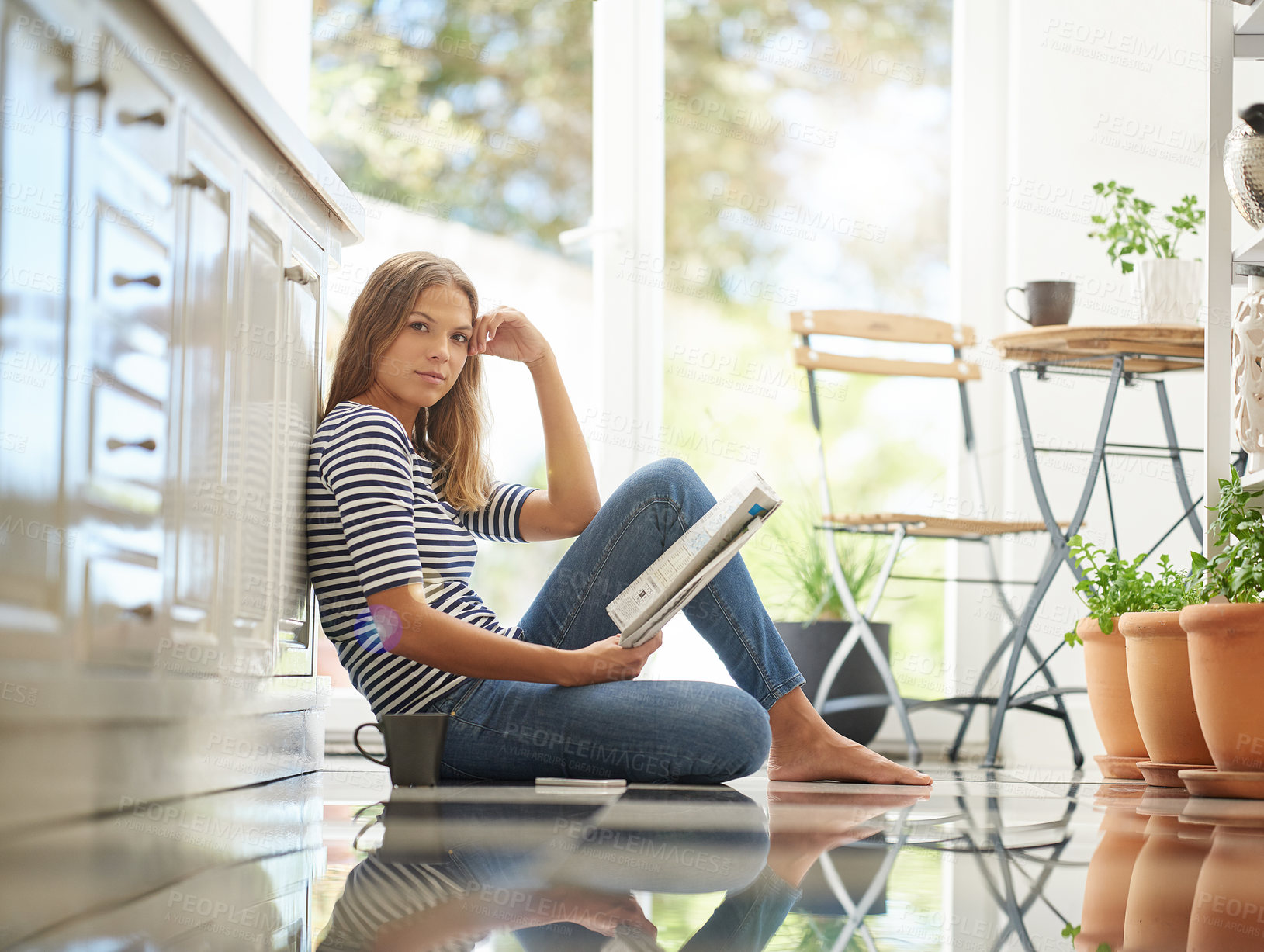 Buy stock photo Portrait of an attractive young woman chilling on her kitchen floor reading a newspaper