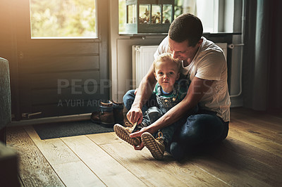 Buy stock photo Shot of a father helping his son put on his shoes at home