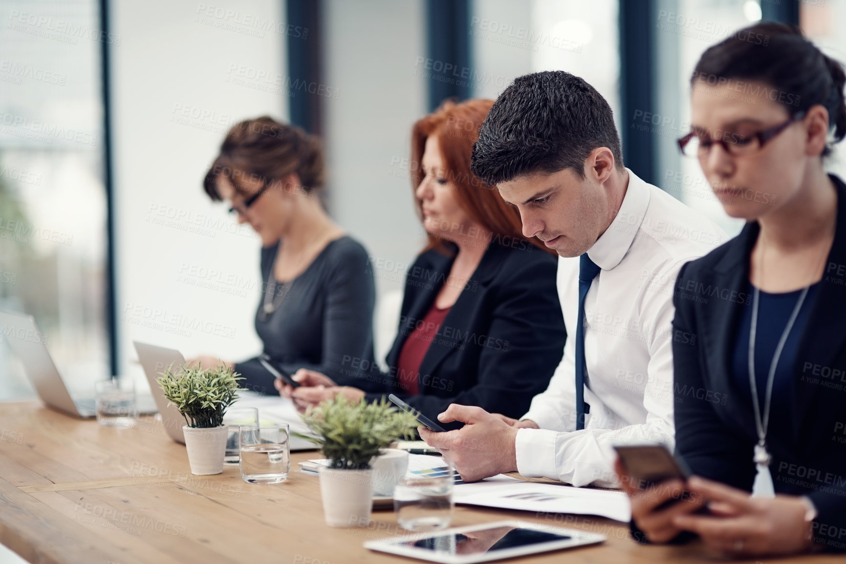 Buy stock photo Cropped shot of a group of businesspeople texting on their cellphones in an office