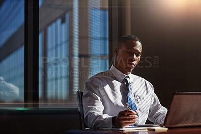 Buy stock photo Shot of a businessman taking notes while using his laptop