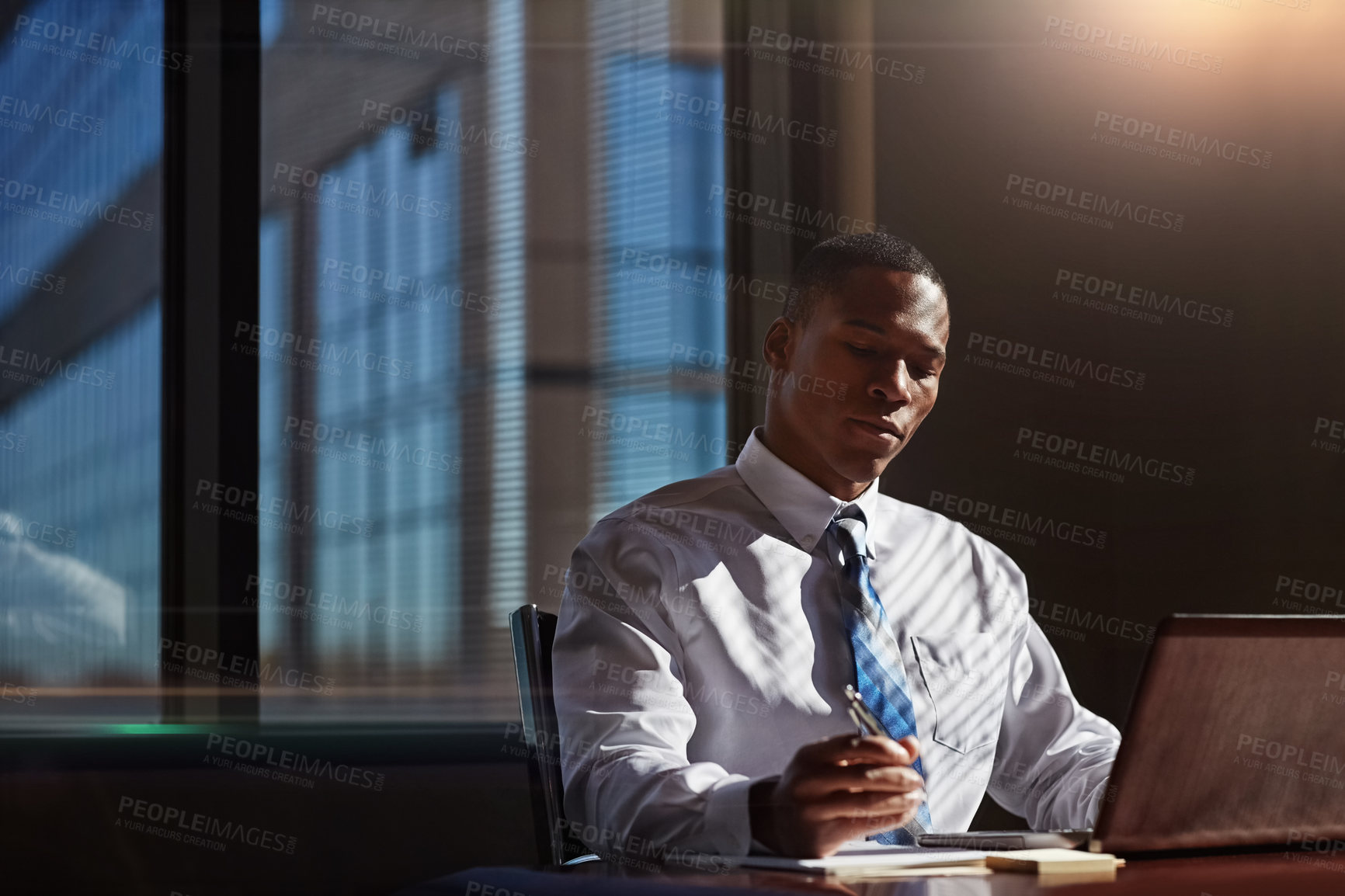 Buy stock photo Shot of a businessman taking notes while using his laptop