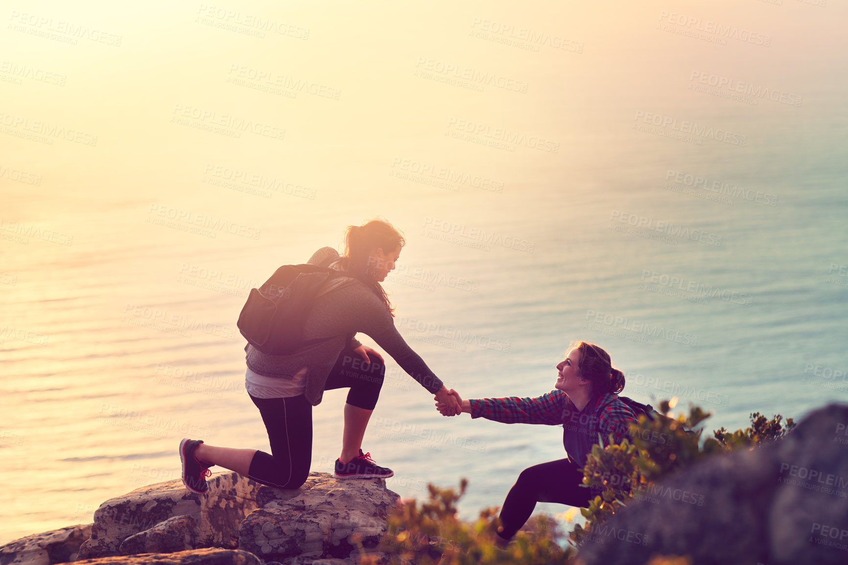 Buy stock photo Shot of a young woman helping her friend up a mountain