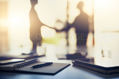 Buy stock photo Closeup shot of a notebook on a desk with businesspeople shaking hands in the background