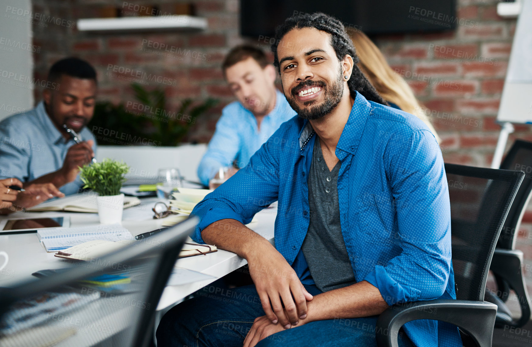 Buy stock photo Portrait of a young designer sitting in an office with his colleagues in the background