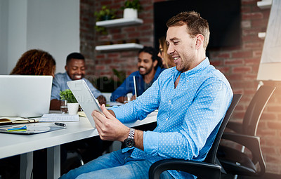 Buy stock photo Cropped shot of a young designer working on a digital tablet with his colleagues in the background