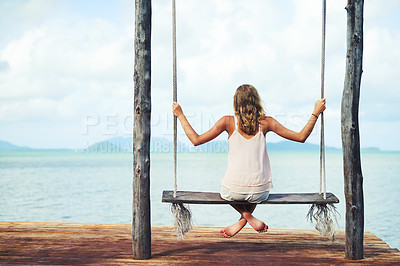 Buy stock photo Shot of a young woman sitting on a swing overlooking the ocean