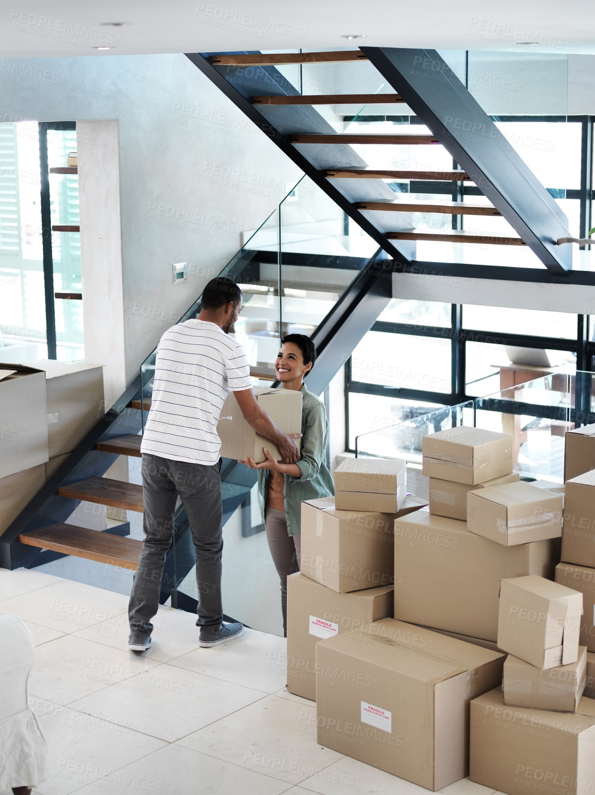 Buy stock photo Shot of a happy young couple passing boxes to each other while moving into their new home