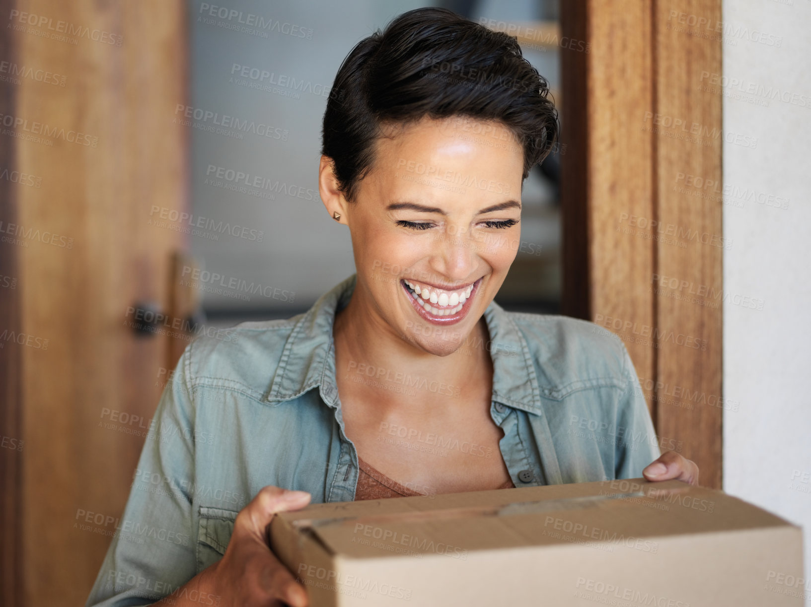 Buy stock photo Shot of a smiling young woman standing at her front door receiving a package from a courier