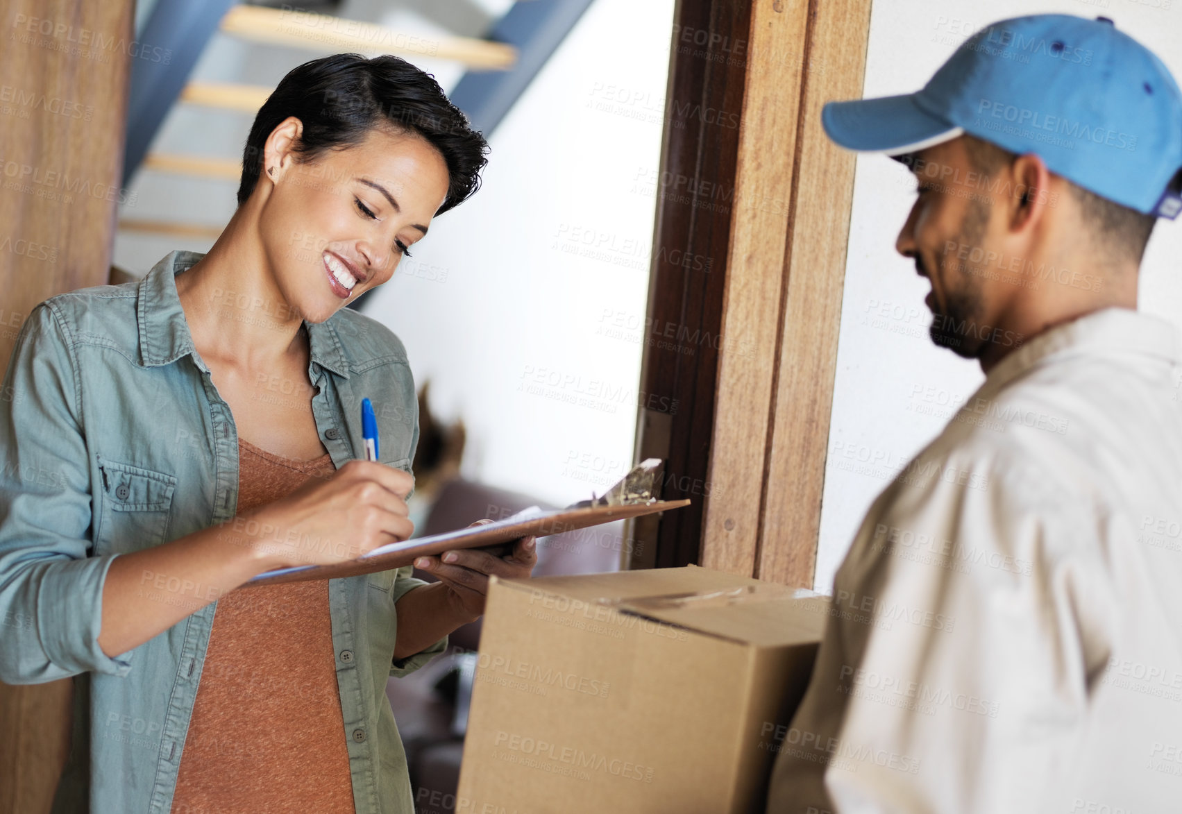 Buy stock photo Shot of a young woman standing at her front door signing for a package from a courier