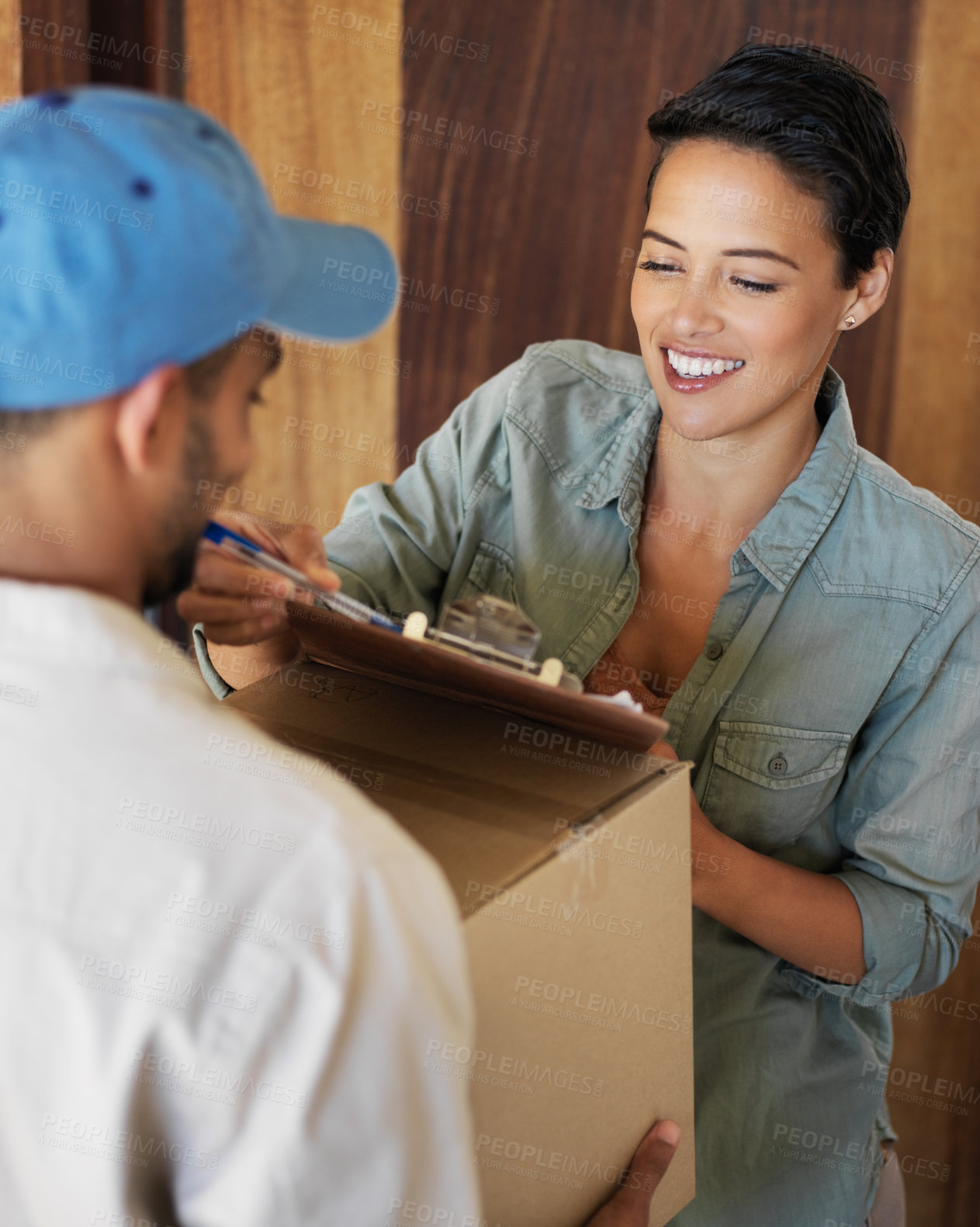 Buy stock photo Shot of a young woman standing at her front door signing for a package from a courier