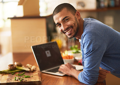 Buy stock photo Portrait of a happy young man using a laptop while preparing a healthy meal at home