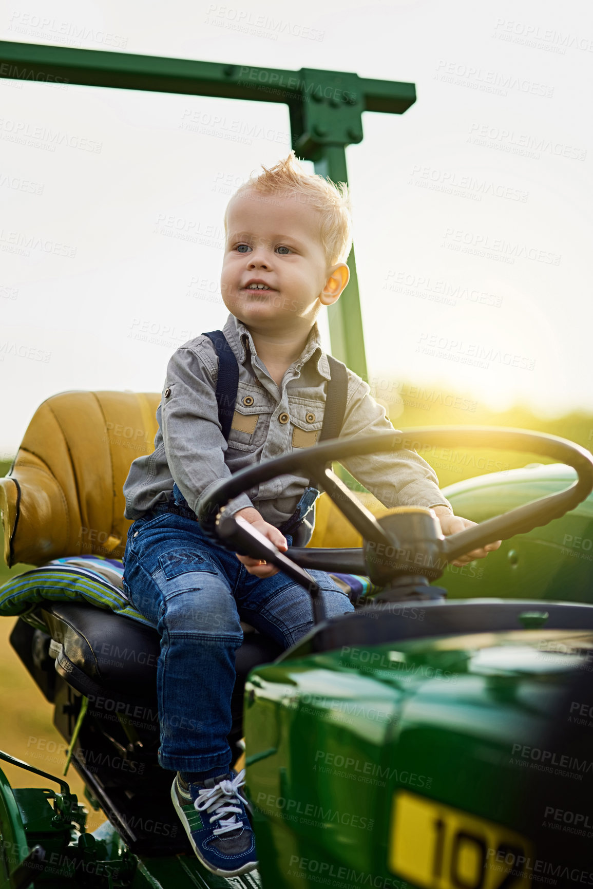 Buy stock photo Boy, kid and driving tractor on farm in countryside for learning agriculture outdoor in nature. Funny child, farmer and play on steering wheel for growth, development and thinking on summer field