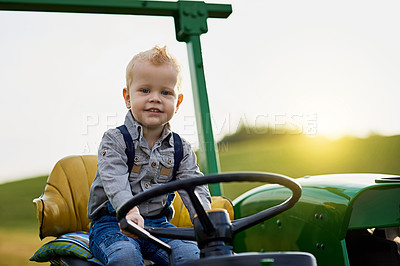 Buy stock photo Portrait of an adorable little boy riding a tractor on a farm