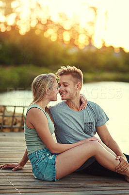 Buy stock photo Cropped shot of an affectionate young couple sitting together at a lake outside