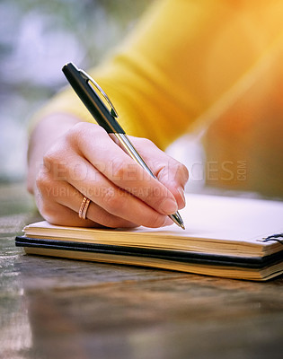 Buy stock photo Cropped shot of a woman sitting at a table and writing in her notepad