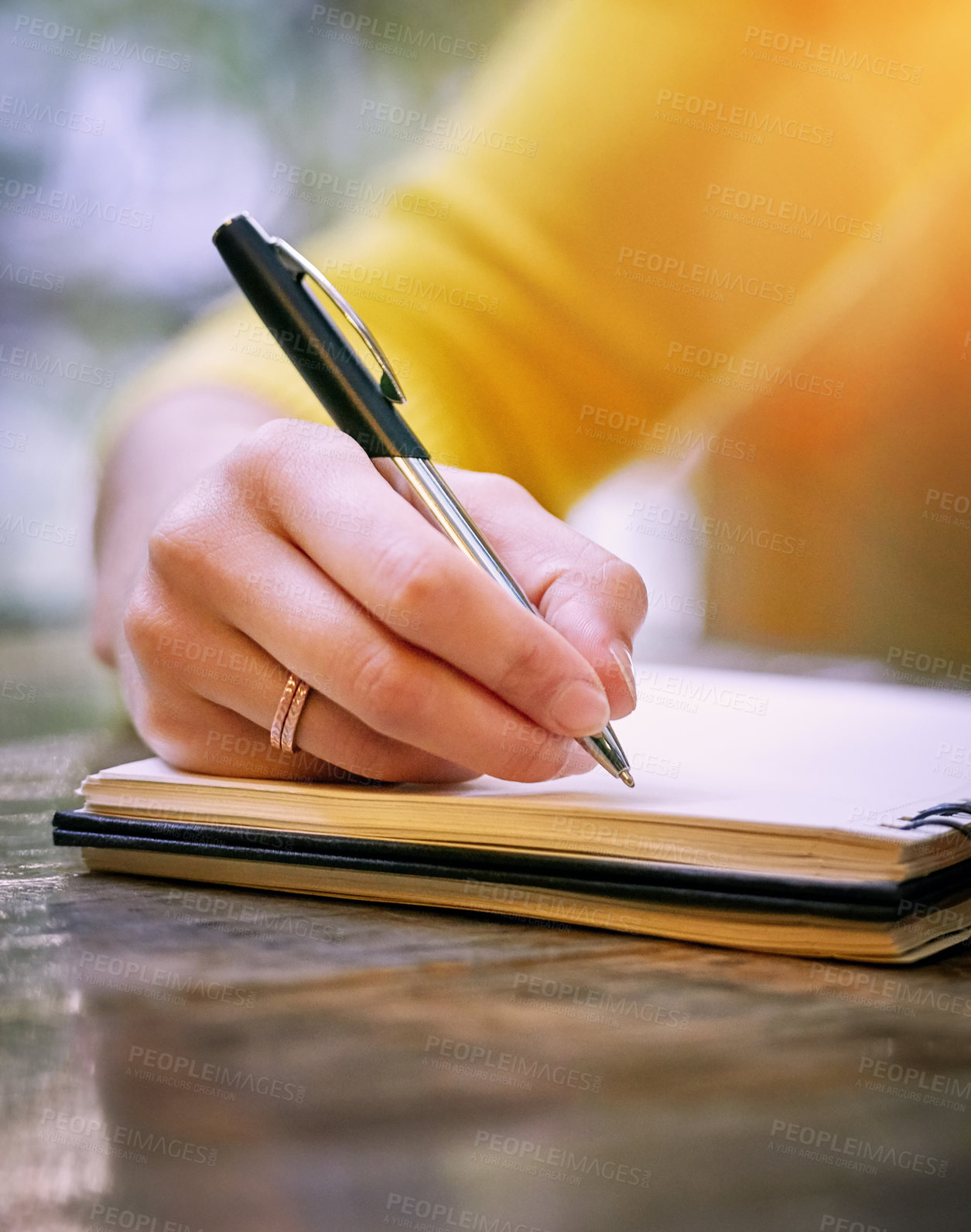 Buy stock photo Cropped shot of a woman sitting at a table and writing in her notepad
