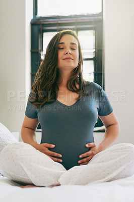 Buy stock photo Shot of a young pregnant woman doing yoga while sitting on her bed