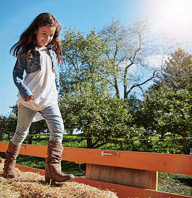 Buy stock photo Shot of a young girl playing on a bale of hay outdoors