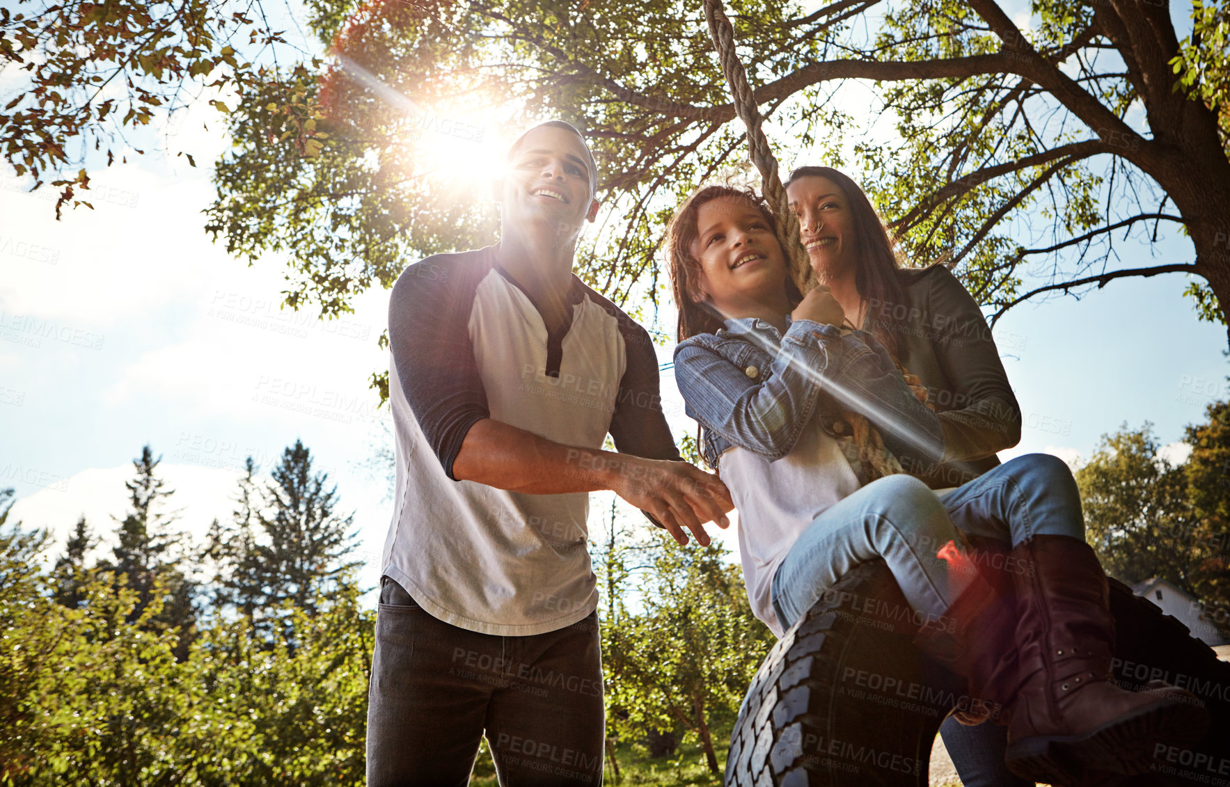 Buy stock photo Parents, girl and happy on tire swing, tree and family with bonding, playful or summer on holiday. People, mom and dad with child, game and flare for push, outdoor fun or excited in countryside