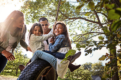 Buy stock photo Shot of a happy mother and  father pushing their daughters on a tyre swing