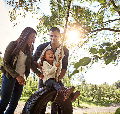 Buy stock photo Shot of a happy mother and  father pushing their daughters on a tyre swing