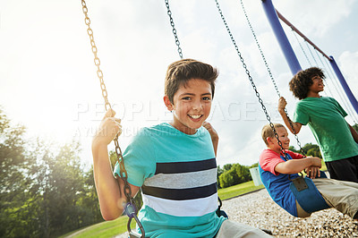 Buy stock photo Portrait of a young boy playing on a swing at the park with his friends