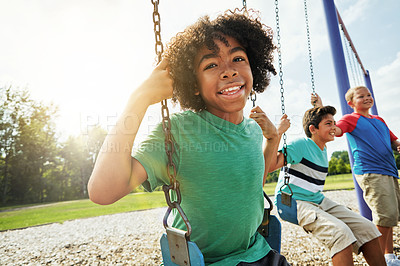 Buy stock photo Portrait of a young boy playing on a swing at the park with his friends