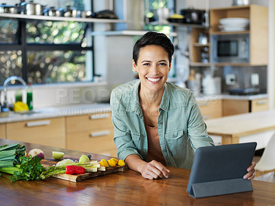 Buy stock photo Portrait of a smiling young woman using a digital tablet while preparing a meal in her kitchen