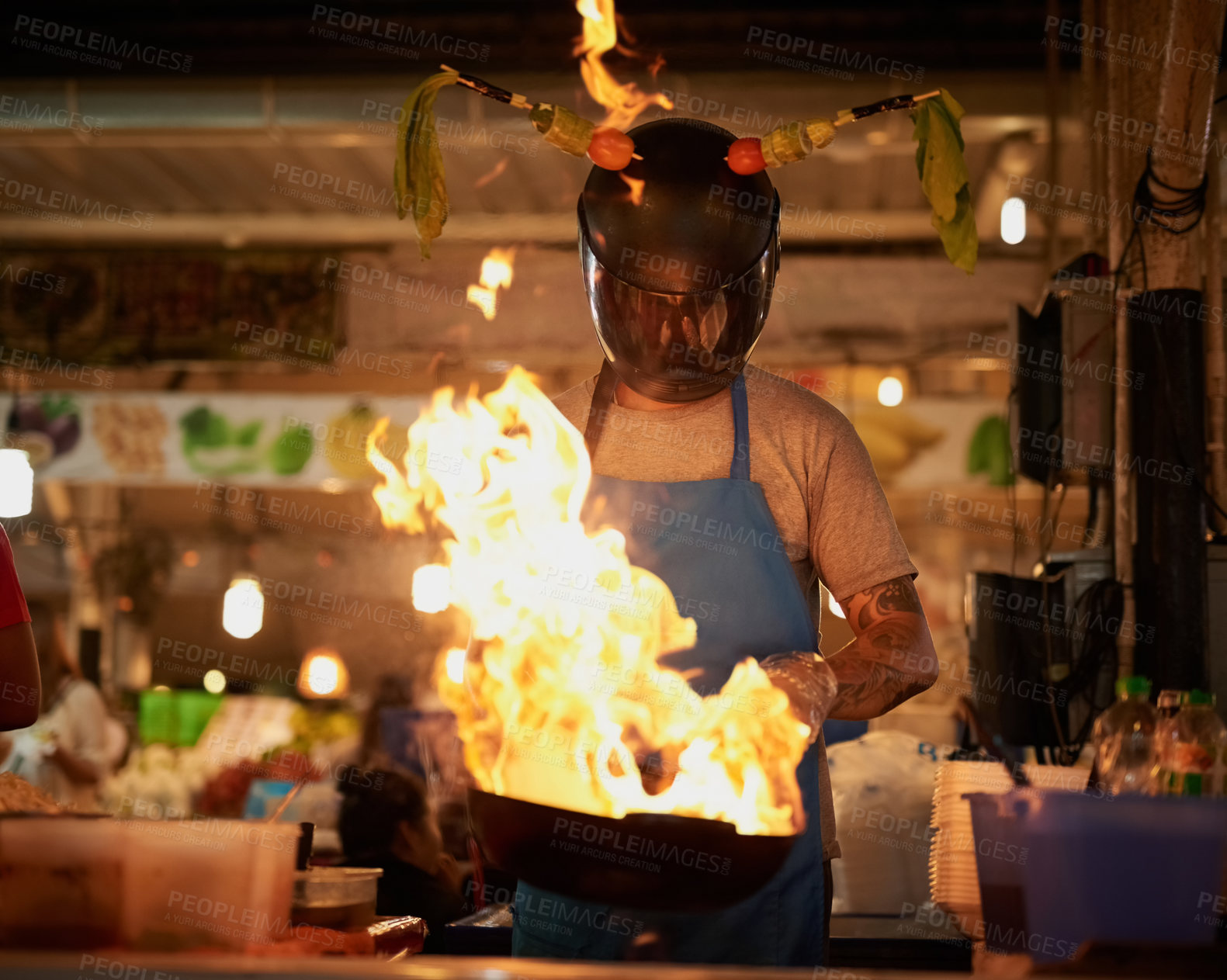 Buy stock photo Shot of an unidentifiable food vendor wearing a helmet while flambeing something in a pan