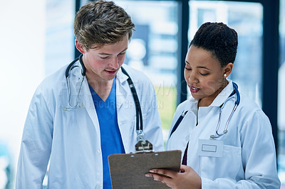 Buy stock photo Shot of two young doctors discussing a patient’s file