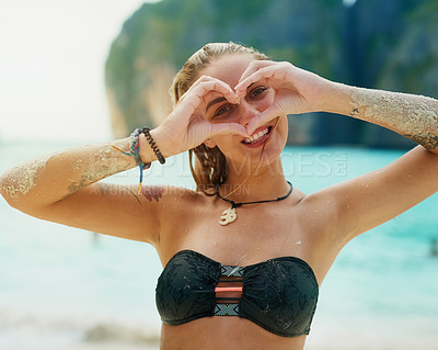 Buy stock photo Portrait of a happy young woman making a heart shape with her hands while swimming in the sea