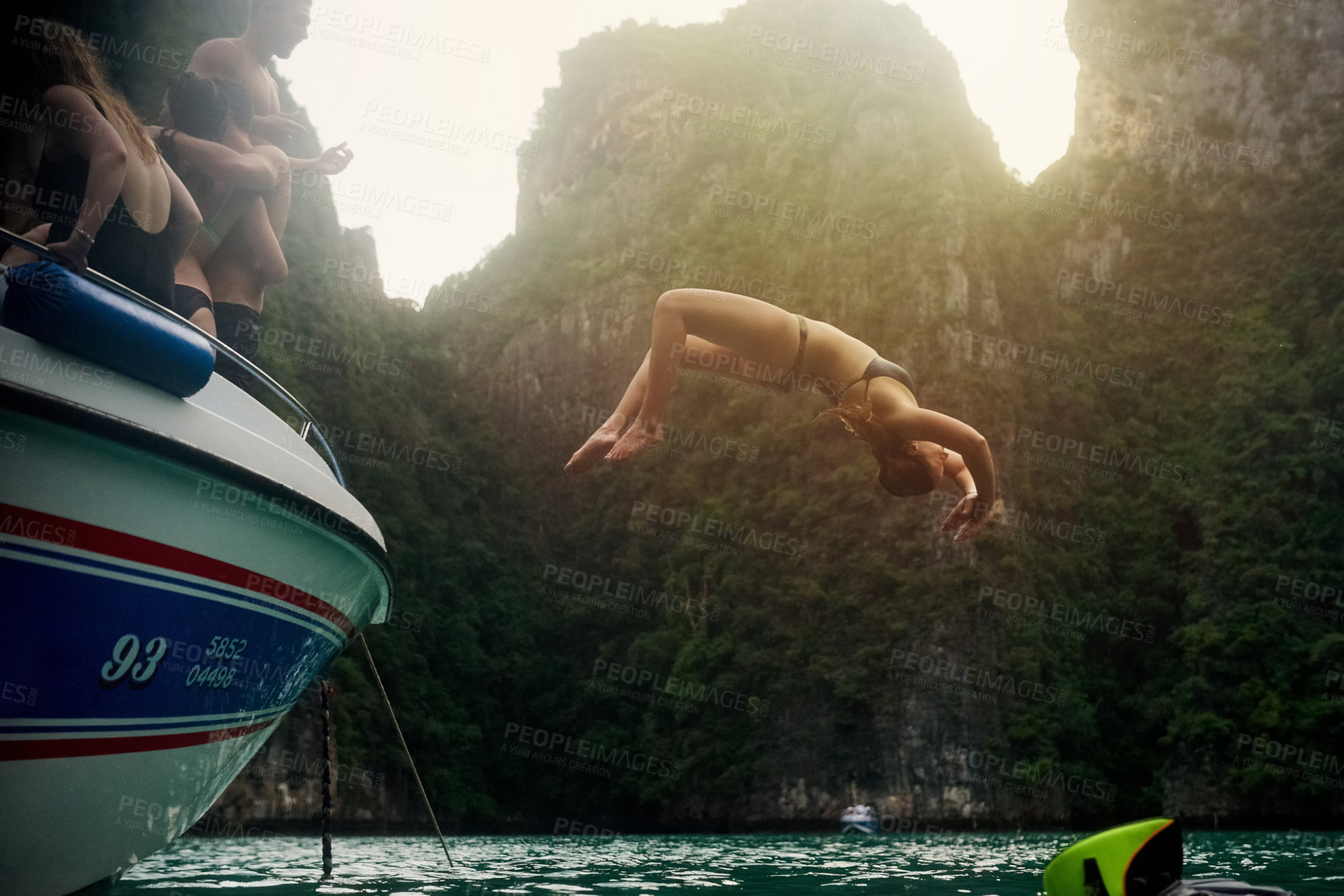 Buy stock photo Shot of a young woman doing a backflip off a boat while her friends watch