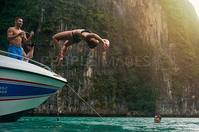 Buy stock photo Shot of a young woman doing a backflip off a boat while her friends watch