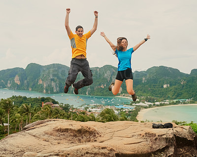Buy stock photo Shot of a happy young couple jumping in front of an island landscape