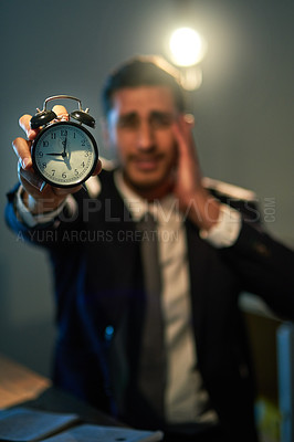 Buy stock photo Shot of a stressed out businessman holding a clock during a late night at work