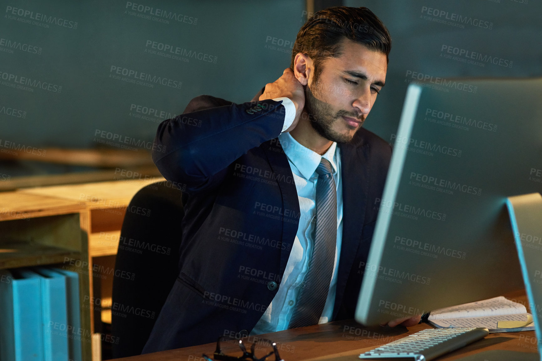 Buy stock photo Shot of a young businessman experiencing neck pain during a late night at work