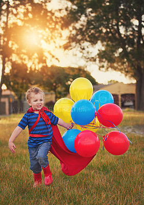Buy stock photo Shot of a cute little boy in a superhero costume carrying a bunch of balloons outside