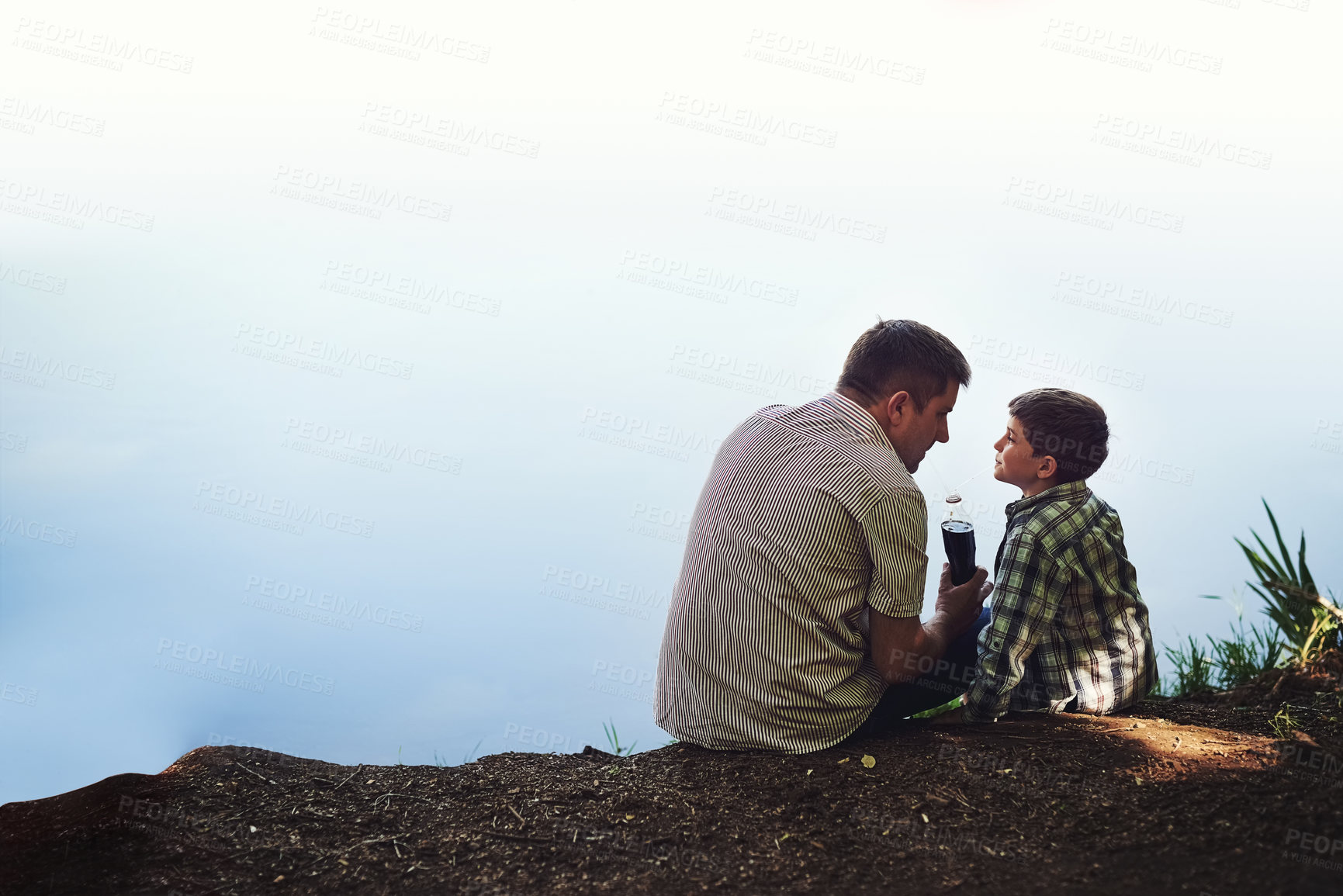 Buy stock photo Shot of a father and his young son sharing a soda while relaxing outside