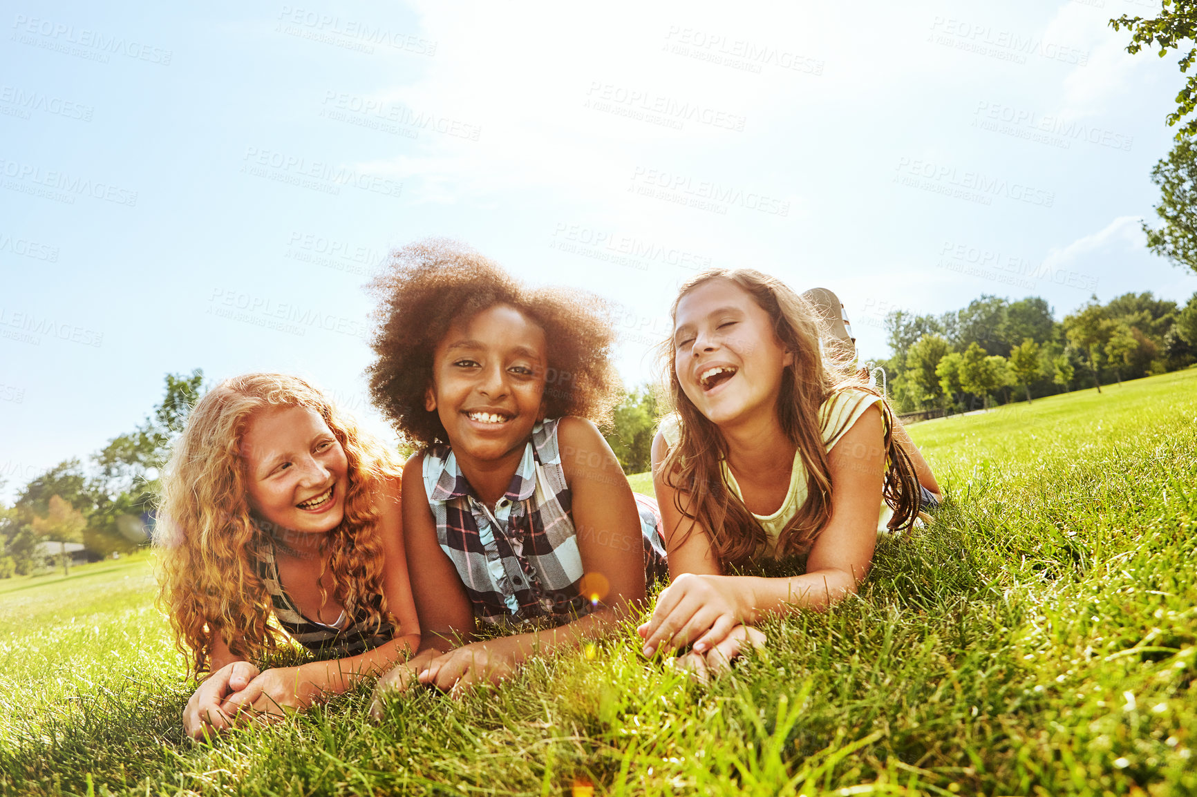 Buy stock photo Shot of three young girls lying together on the grass outside