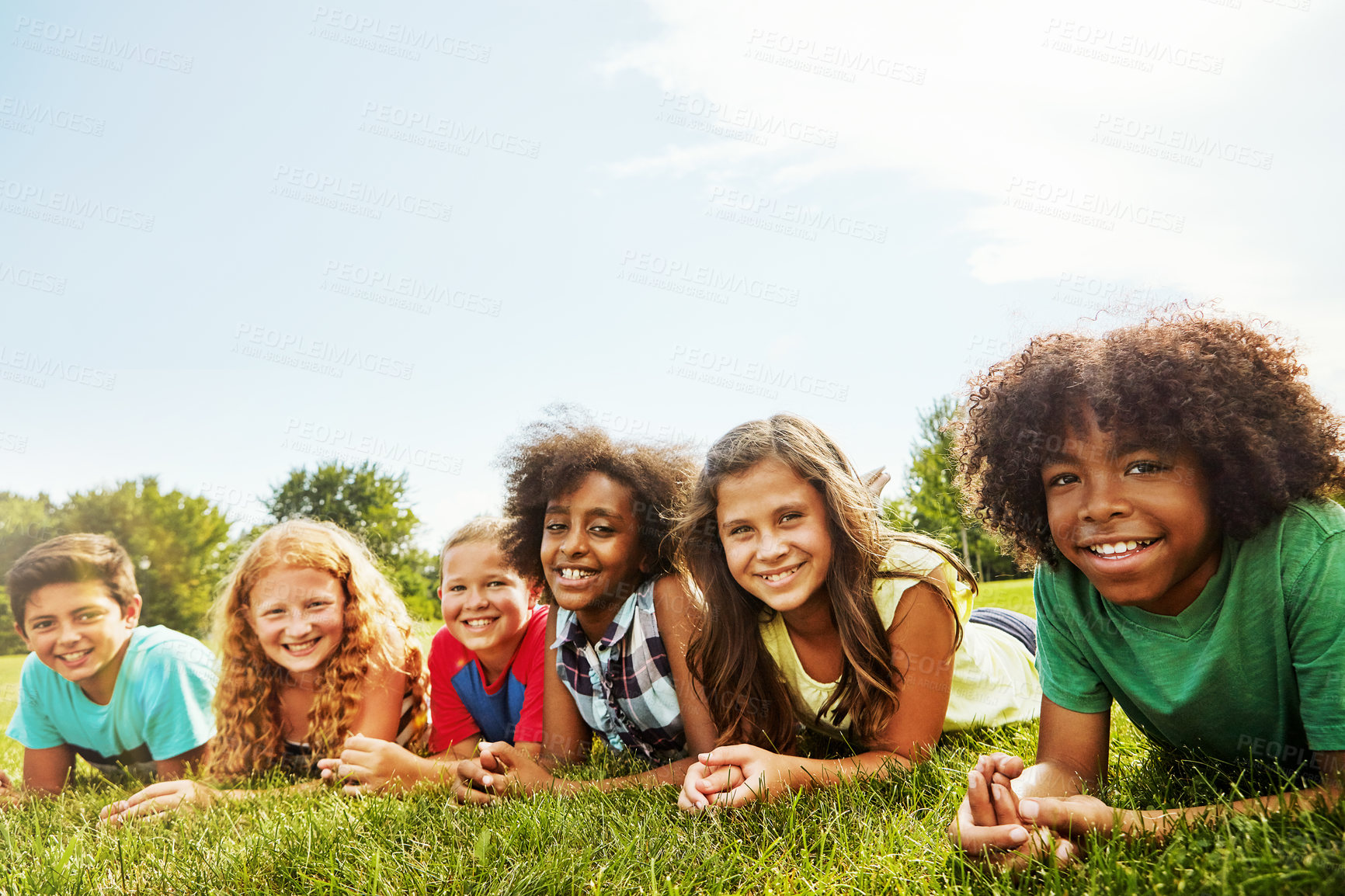 Buy stock photo Portrait of a group of diverse and happy kids lying together on the grass outside