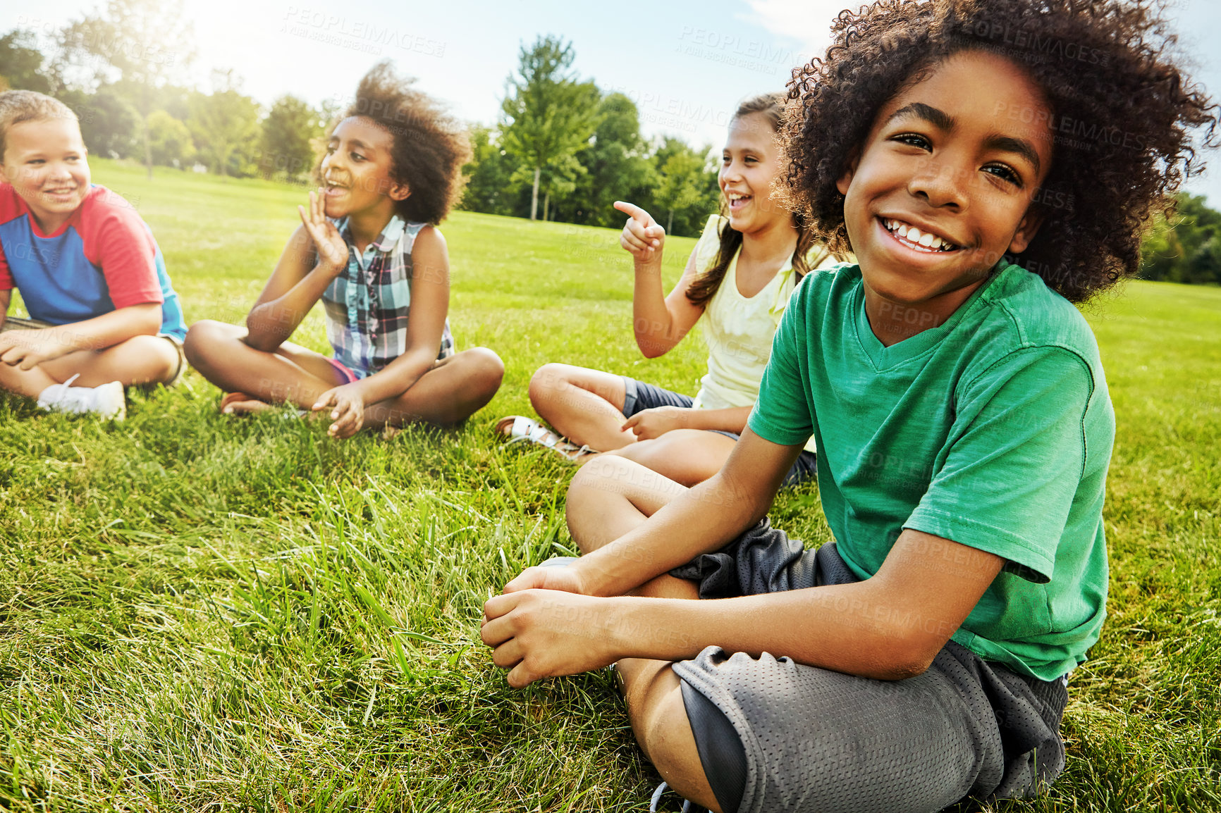 Buy stock photo Portrait of a young boy sitting together with his friends on the grass outside