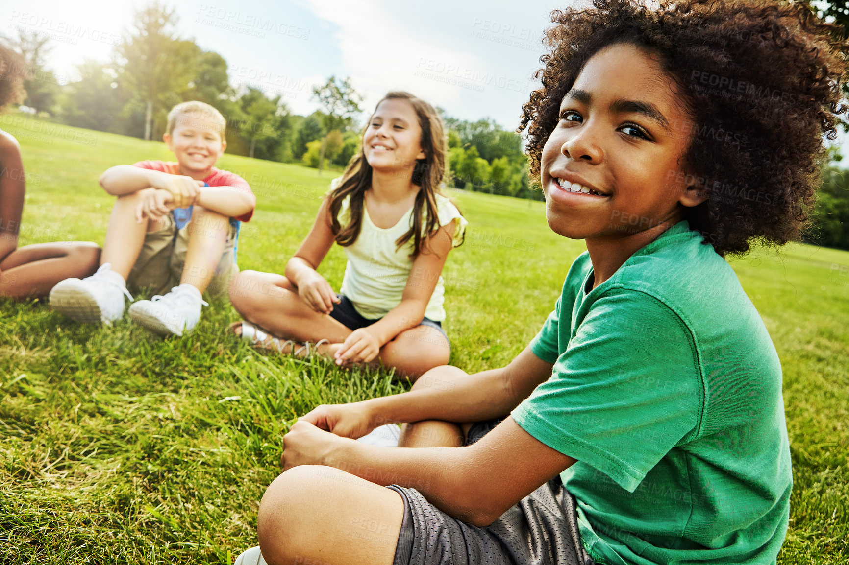 Buy stock photo Portrait of a young boy sitting together with his friends on the grass outside