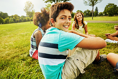 Buy stock photo Portrait of a young boy sitting together with his friends on the grass outside