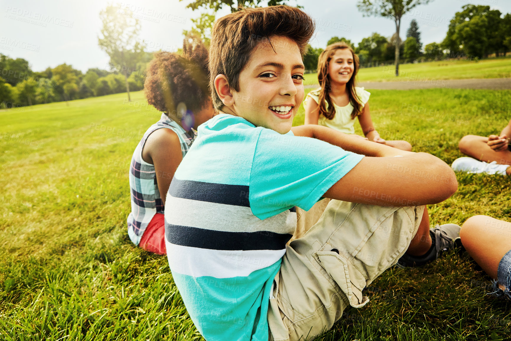 Buy stock photo Portrait of a young boy sitting together with his friends on the grass outside