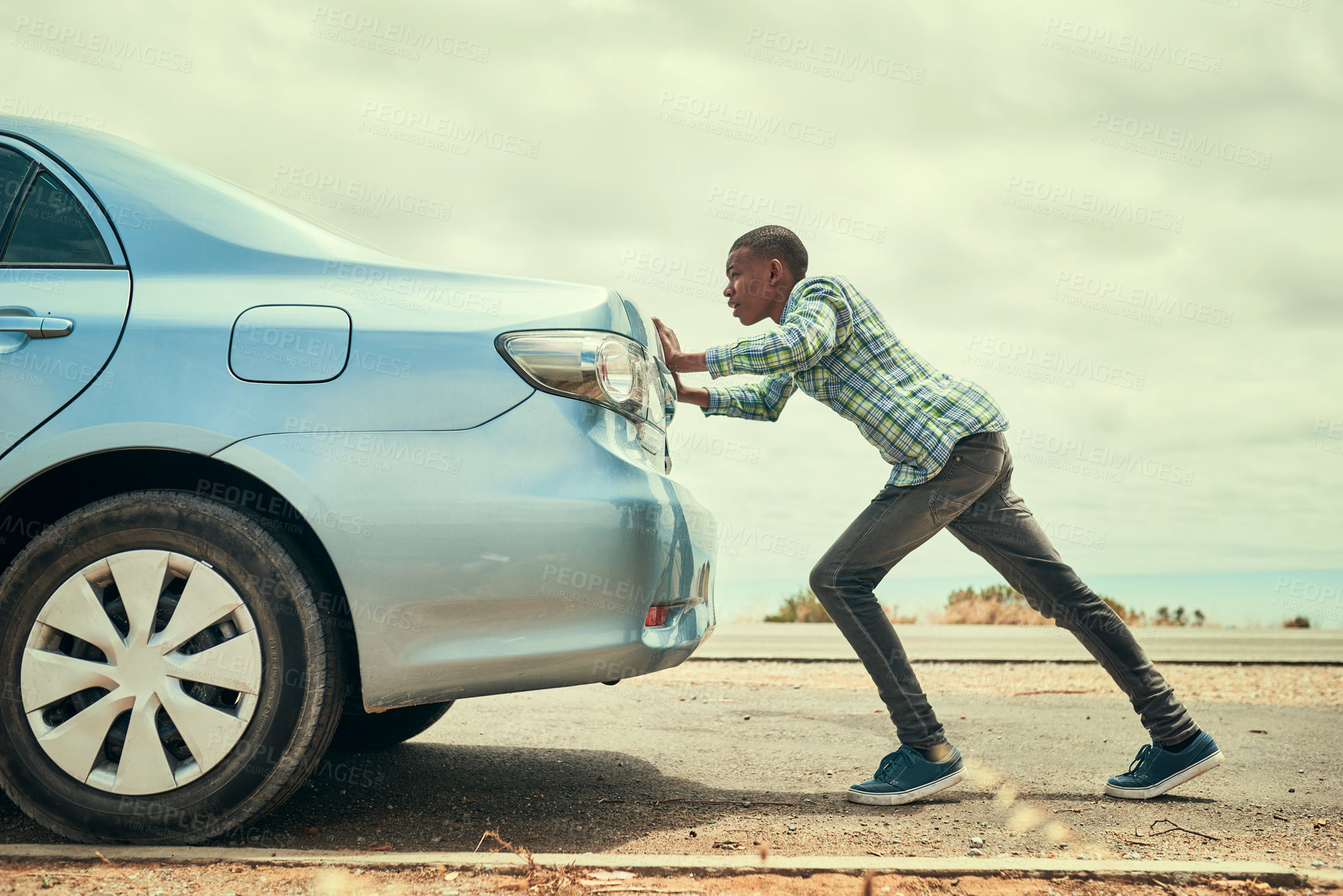 Buy stock photo Full length shot of a young man pushing his car along the road after breaking down
