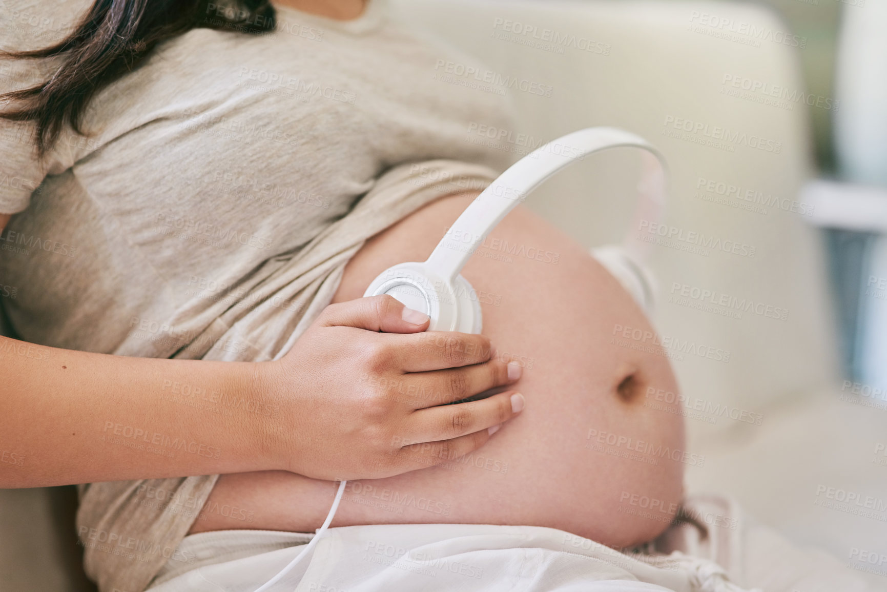 Buy stock photo Shot of a woman wearing headphones over her pregnant belly