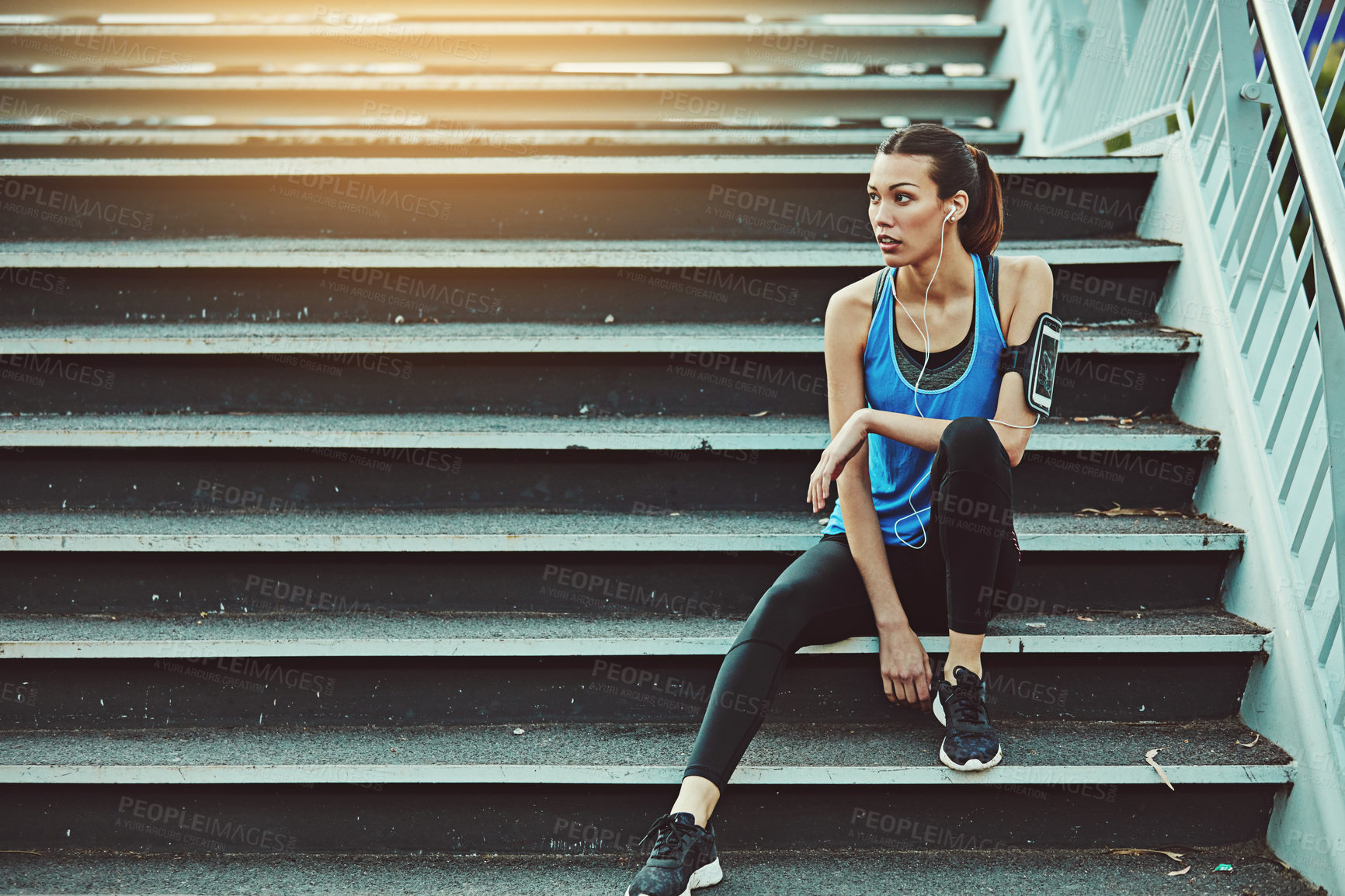 Buy stock photo Shot of a sporty young woman listening to music while sitting on a staircase