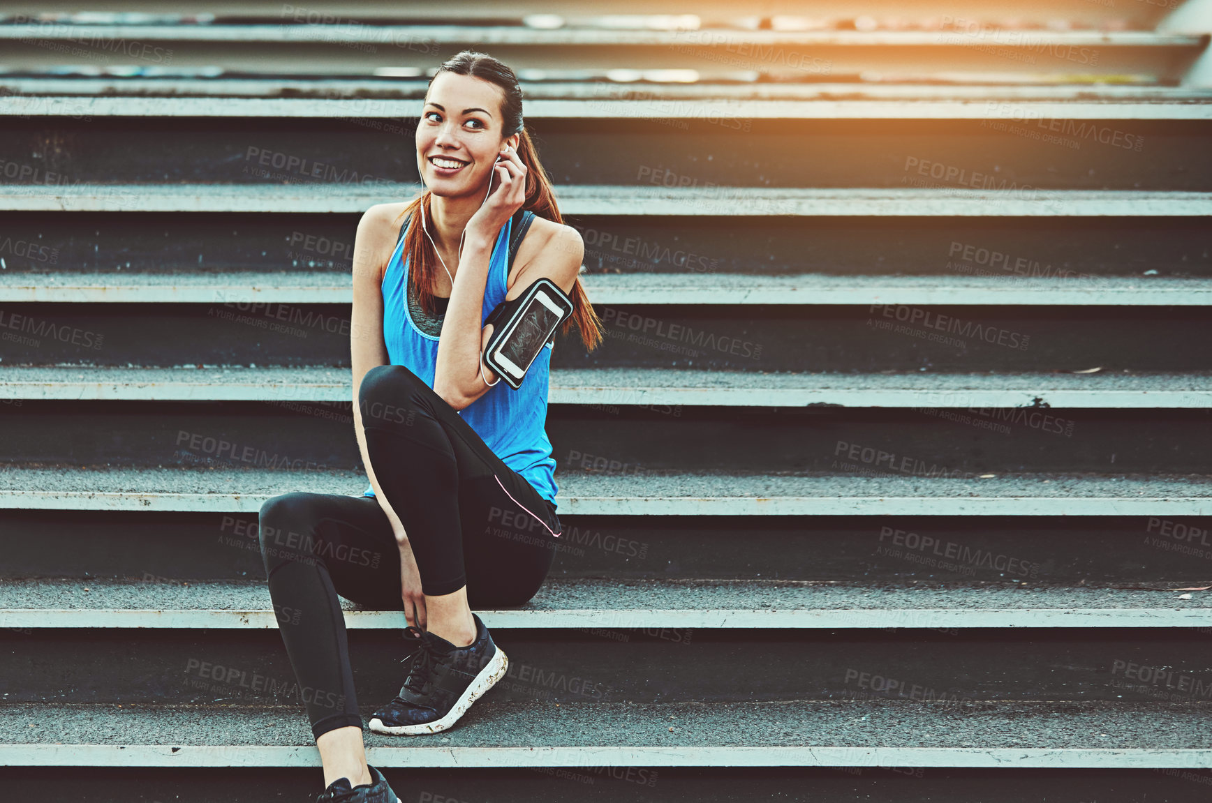 Buy stock photo Shot of a sporty young woman listening to music while sitting on a staircase