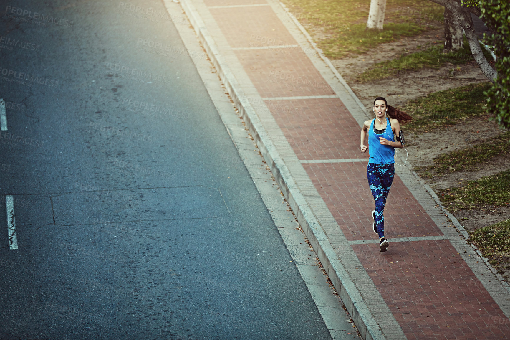 Buy stock photo Girl, running and fitness in street, city and listen to music with above with earphones in summer. Woman, runner and space for audio streaming, exercise or training with smartphone on road in town